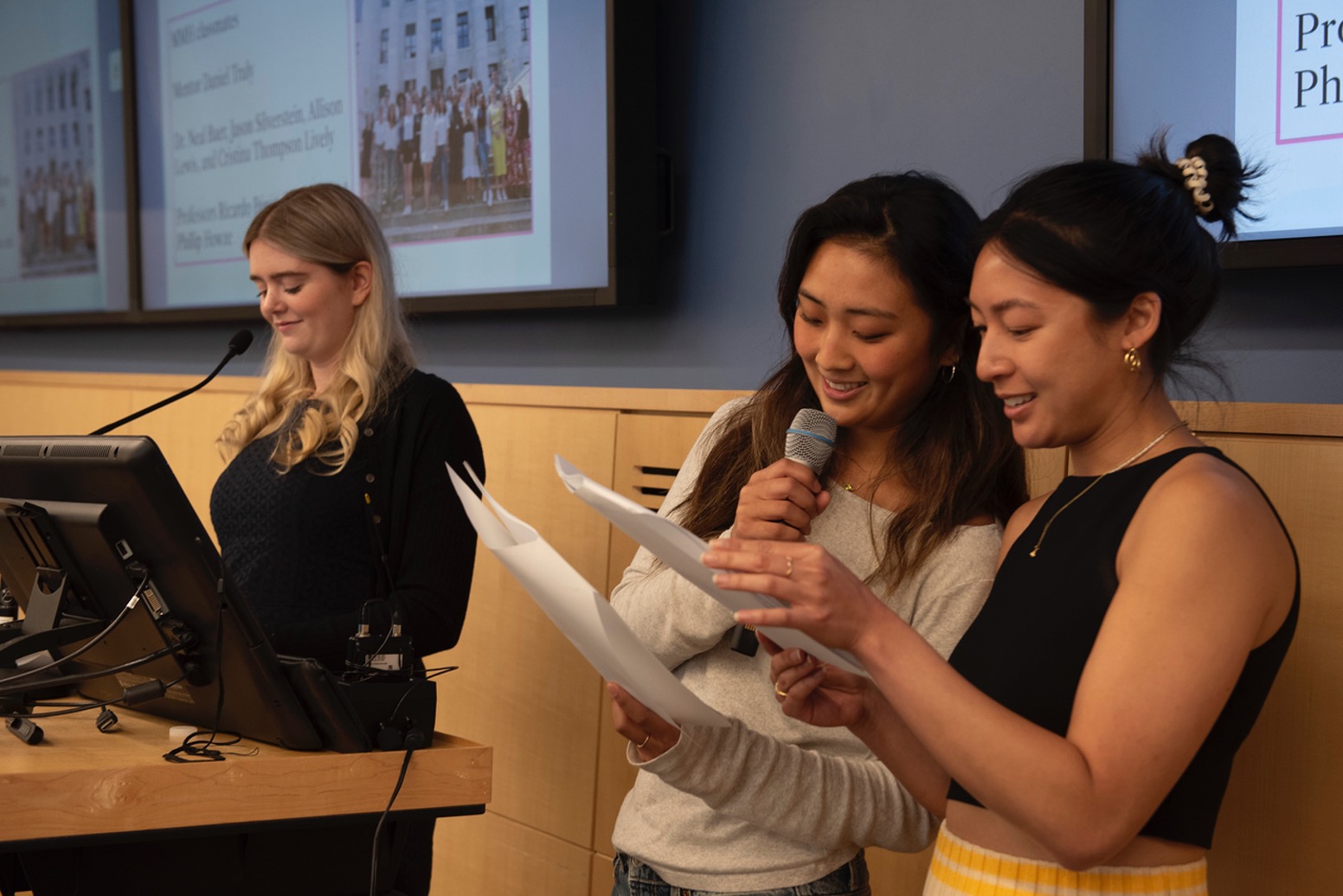 Clare speaks on the podium next to two students acting her script