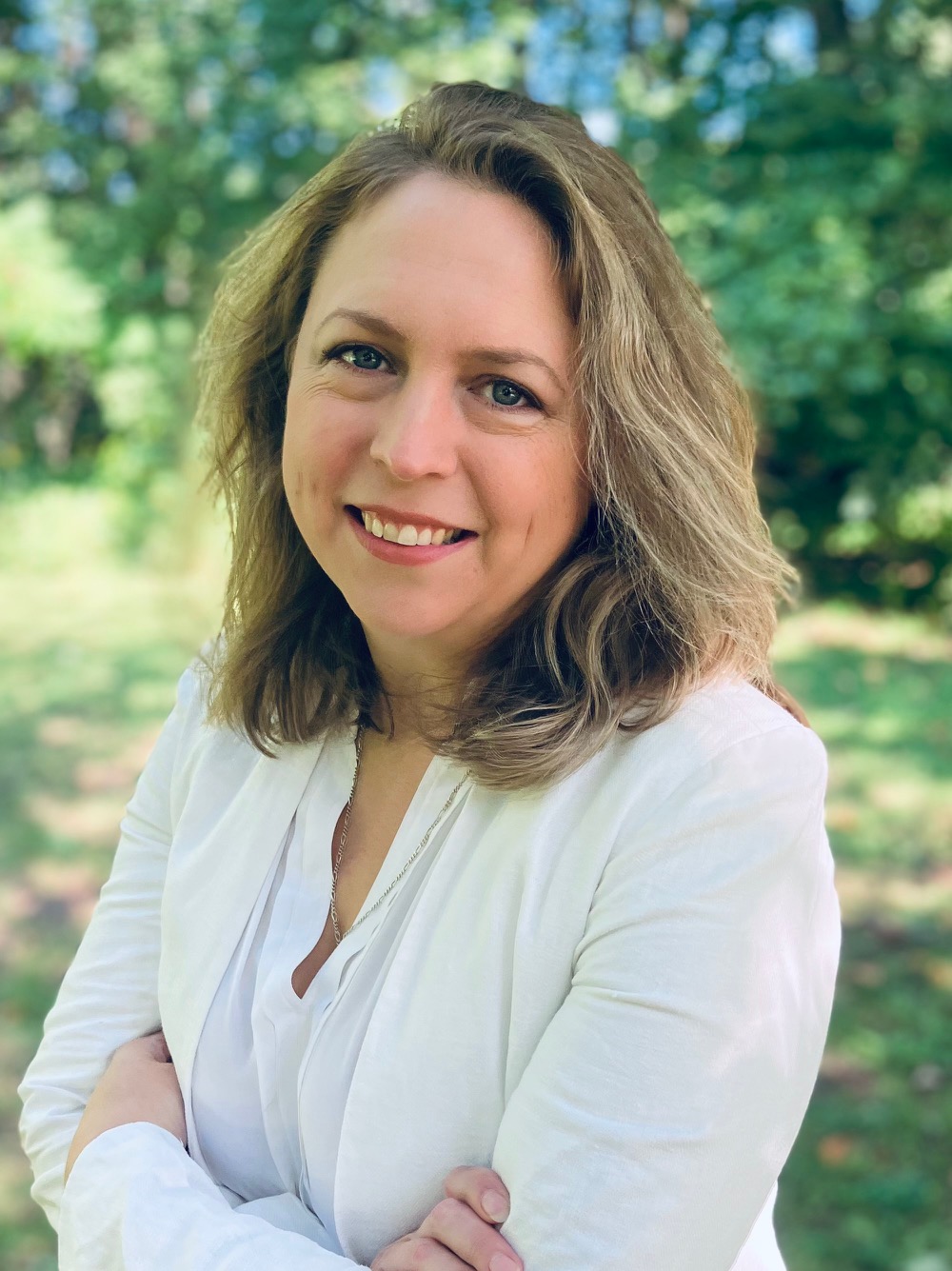 headshot of Victoria Brown, smiling, arms crossed, outdoor springtime setting