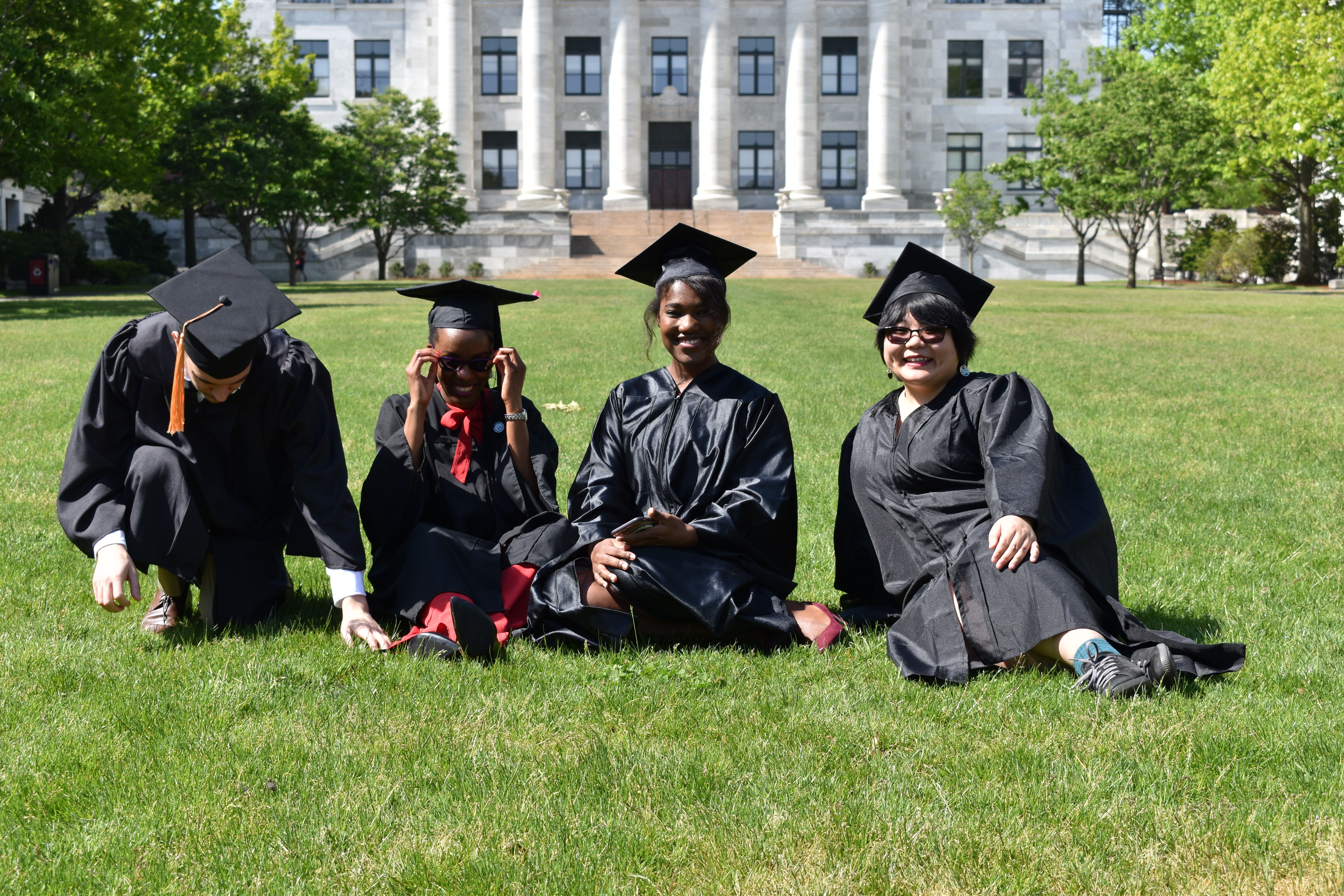 Group of people in graduation regalia sitting on a lush lawn.