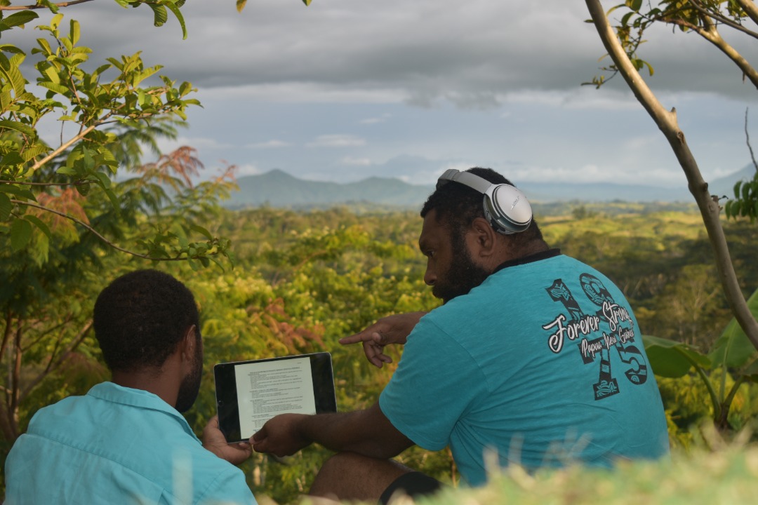 Two men discussing data on an Ipad with a lush background of trees and mountains beyond them