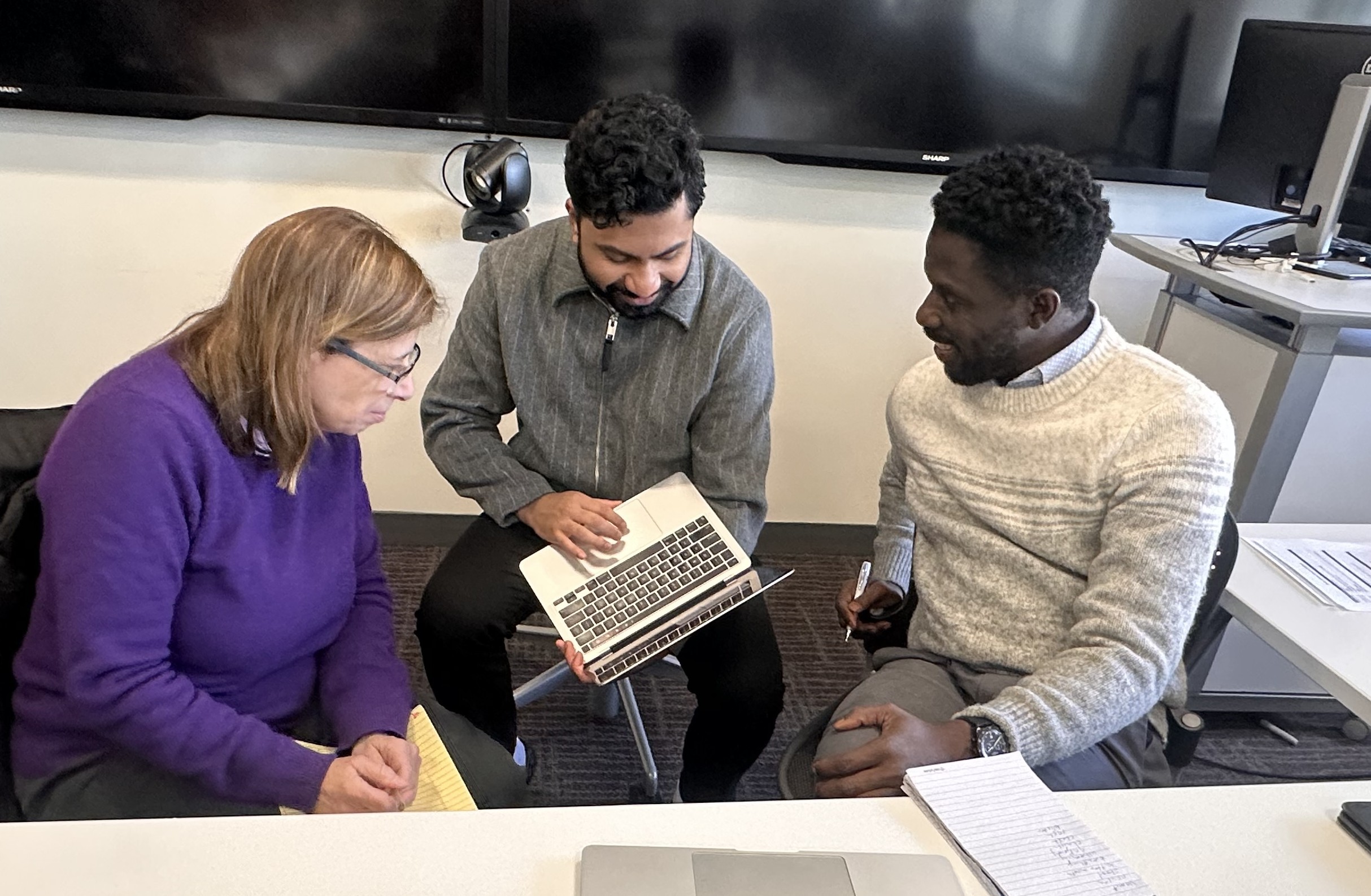 Three people look at a project on a laptop 