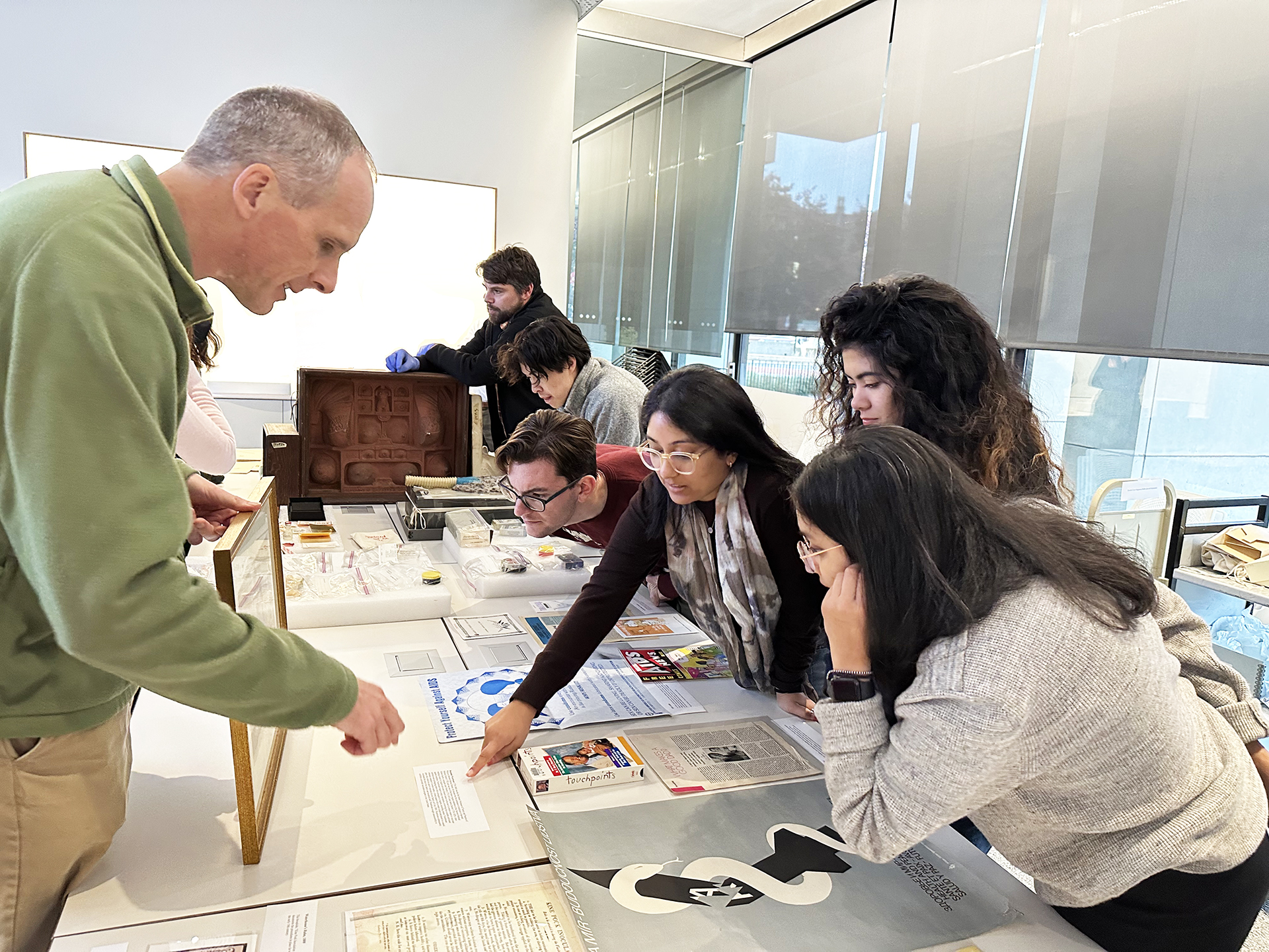 People stand around a table looking at artwork and documents on the table. 