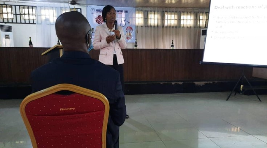 Egbe giving a talk presentation with a microphone in her hand. There is one man seated watching her. 