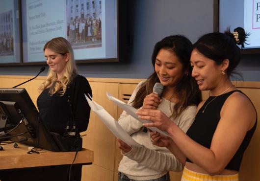 Clare speaks on the podium next to two students acting her script
