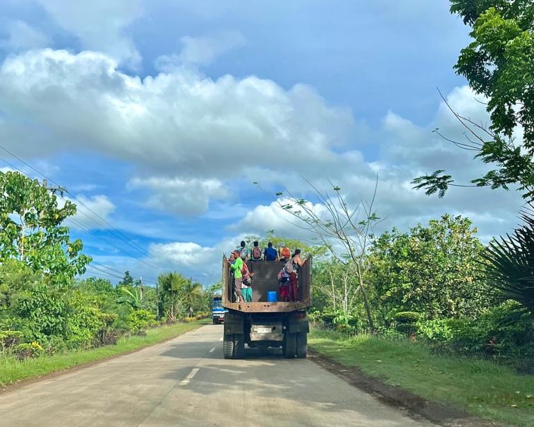 People riding on an open truck on a dirt road