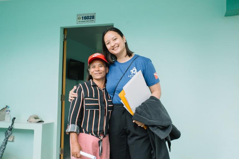 Two women standing together in front of a green building