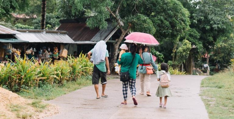 Women with children and umbrellas walking on a dirt road