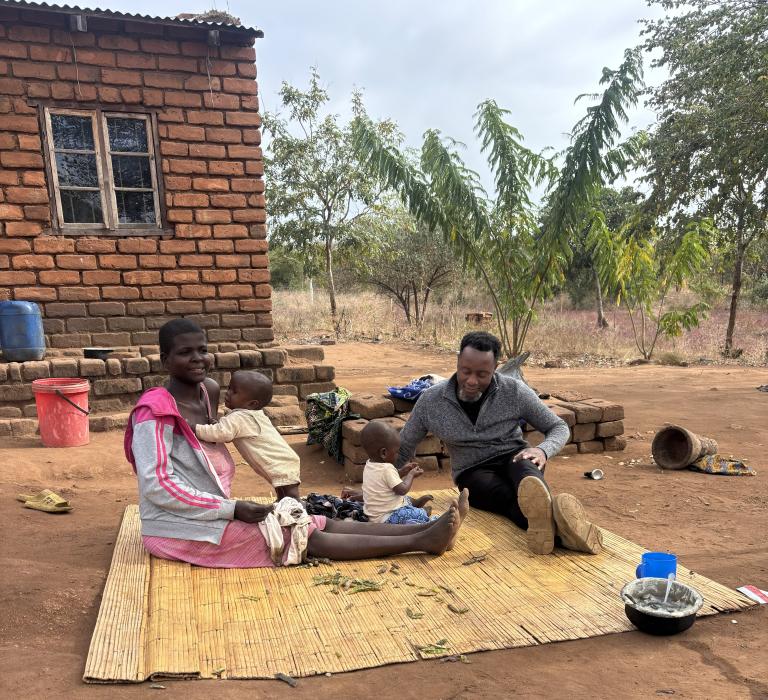 two adults and one child sit on a mat in Malawi