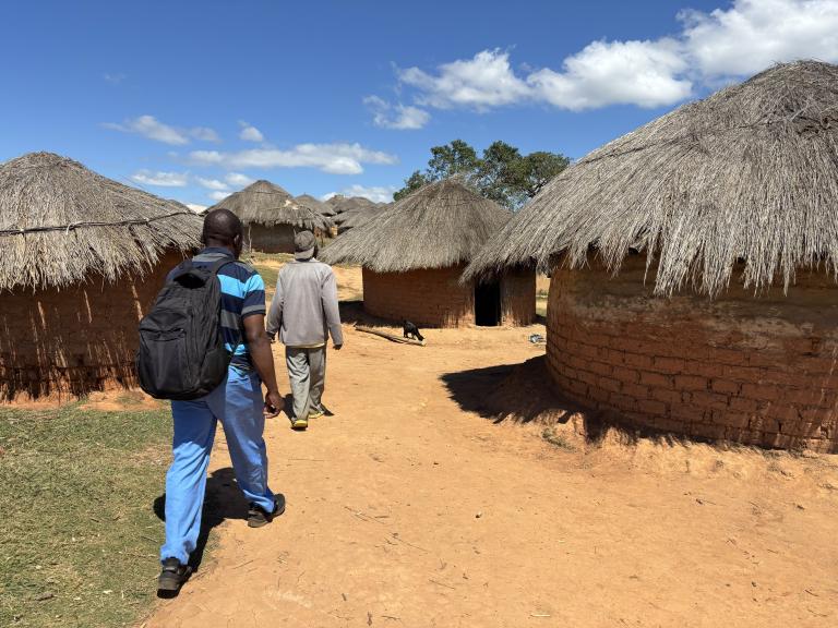 Two people walk through a village in Malawi