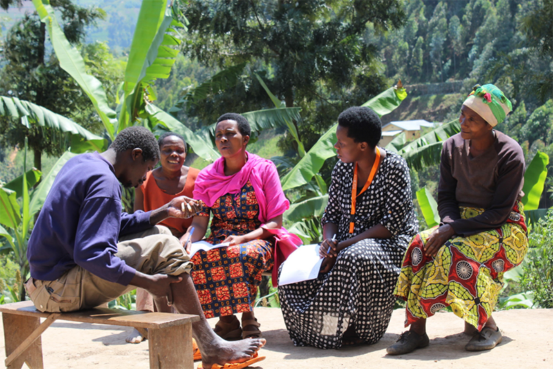 Hategekimana Bashar (left), members of his family, and Mental Health Social and Community support Coordinator Sifa Dorcas (second from right) chat outside Bashar’s home in Rwanda in 2016. Photo by Bob Muhumuza.